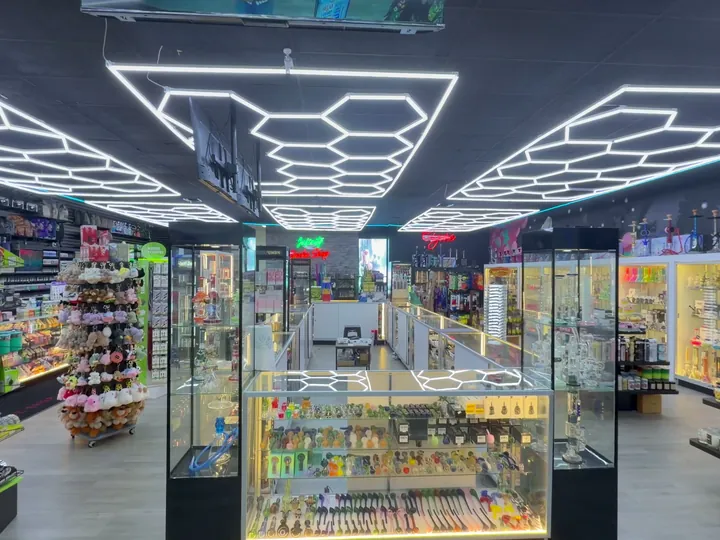 Main aisle under hexagon ceiling lights, with a long glass counter, tall display towers and neon signs