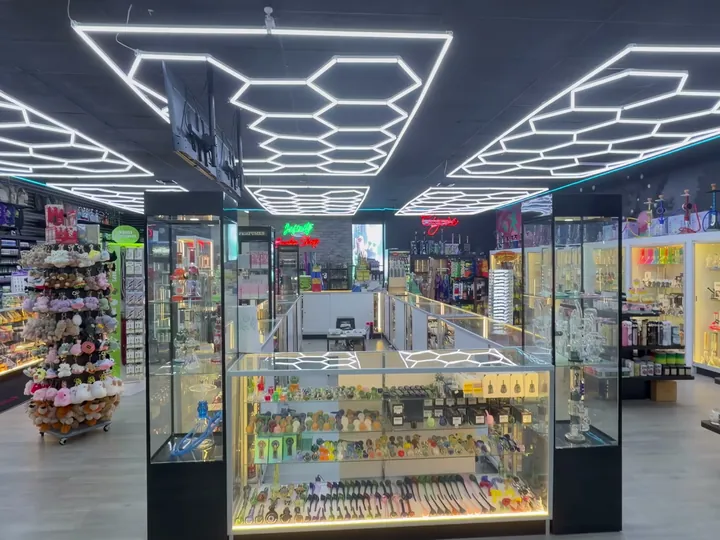 Center aisle under hexagon ceiling lights, with a lit case of glass hand pipes and wall cases