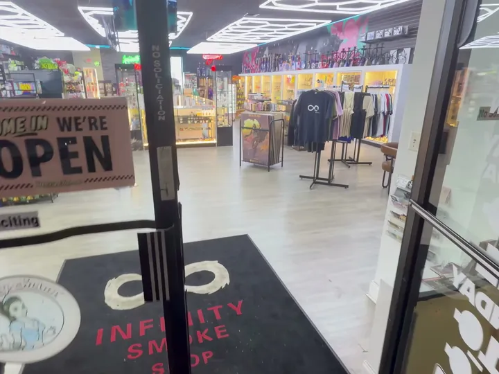 View through the open glass front door, with an open sign and the infinity logo mat inside