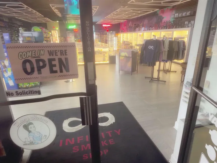 Looking through the open front door at the shop floor, with an open sign on the glass and the logo mat