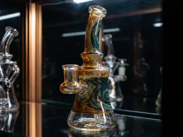 Amber and teal swirl glass water pipe on a lit glass shelf inside a dark display case