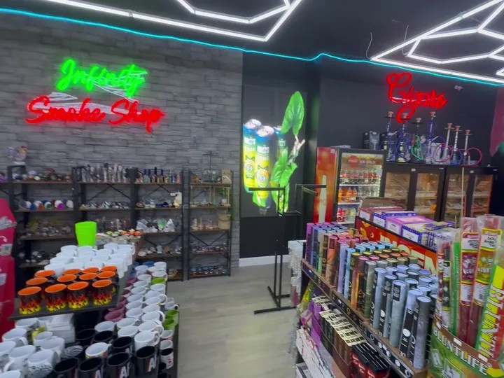 Neon Infinity Smoke Shop sign on a stone wall, with a Cigars sign over hookahs and cabinets